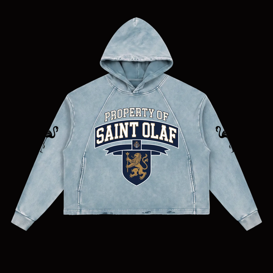 A light blue acid-wash cropped hoodie featuring a 'PROPERTY OF SAINT OLAF' graphic with a lion crest on the front, and black snake graphics on both sleeves, shown against a plain white background.